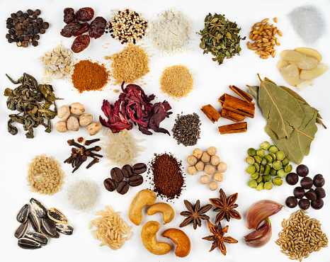 Overhead view of food ingredients  .  The food ingredients are: brown rice, white rice, rolled oats, yellow peas, chickpeas, split peas, salt, shredded coconut, chocolate chips, sesame, slivered almonds, cashew,  quinoa, coffee beans, raisins, whole wheat, cinnamon stick hibiscus flower, green tea, star anise, cloves, ground coffee, black peppercorns, oregano, garlic cloves, wheat flour, garlic powder, brown sugar, birdseed, bay leaves, sunflower seeds. Image made in studio