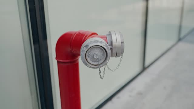 Red fire hydrant pipe stands on street near windows of office building closeup