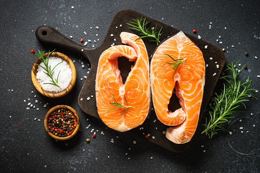Salmon steaks on cutting board at black background. Top view with ingredients for cooking.