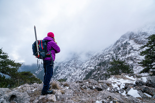Female mountain climber is looking at the landscape and the summit of a high altitude mountain while standing arms crossed.