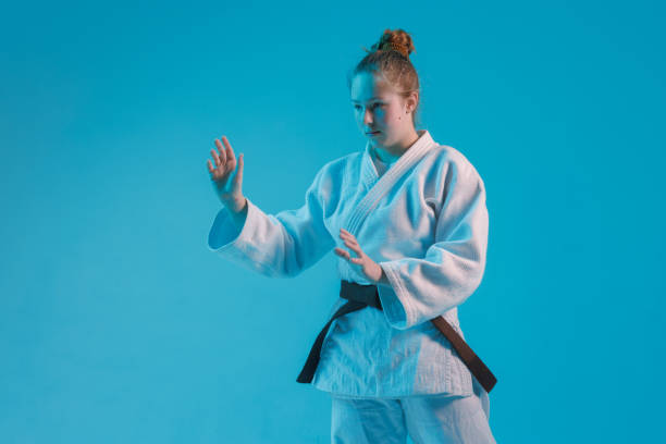 fille judoka dans un kimano blanc avec une ceinture noire sur un fond bleu, photo de studio - martial arts women tae kwon do black belt photos et images de collection