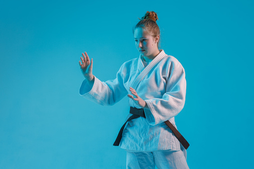 girl judoka in a white kimano with a black belt on a blue background, studio photo