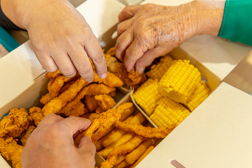 closeup of three hands taking food from a fast food box with chicken, corn, french fries and arepas