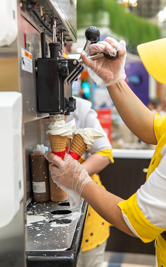Close-up of unrecognizable person in yellow clothing serving ice cream from an ice cream machine