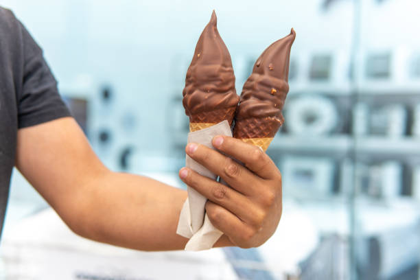 istock Man's hand holding two chocolate covered ice cream sundaes 1970955663