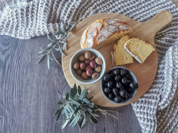 Table view consisting of several bowls with different types of olives, plate with cornbread and extra virgin olive oil, dark wood table background and olive branches...