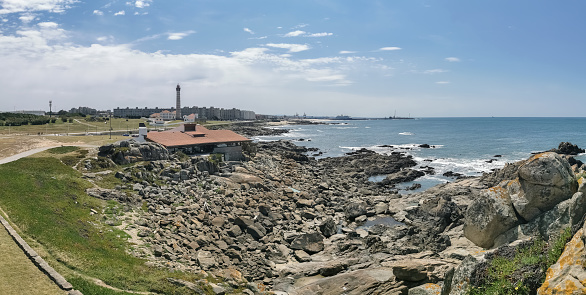 View at the Blue Beach or praia Azul and Casa de Chá da Boa Nova, a building Built on the rocks, front to the sea, Leça da Palmeira urban buildings and lighthouse as background...