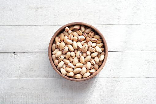 Pistachios in bowl on white wooden background