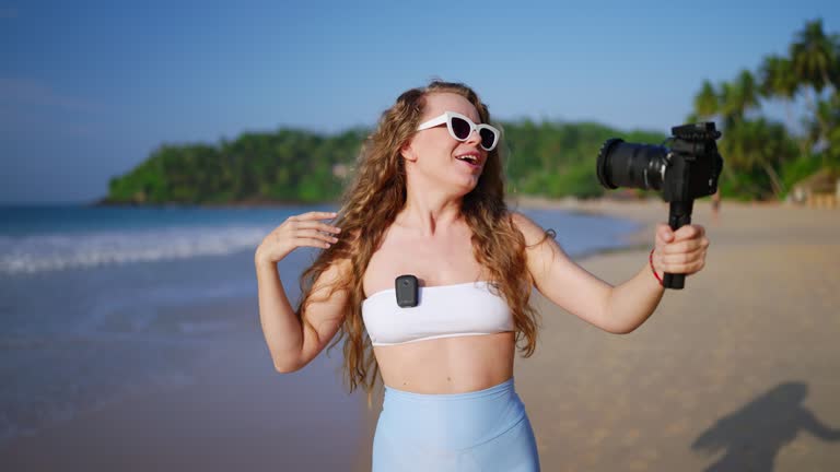 Travel influencer films beach vlog using pro camera, lav mic, sharing tips, capturing scenic landscape, engaging viewers with journey, earning through content creation exploring tropical coast. Slowmo