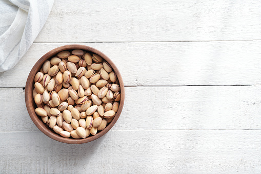 Pistachios in bowl on white wooden background