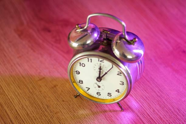 Vintage alarm clock on a wooden floor. Illuminated with vibrant pink light. Night time metaphor. Selective focus.