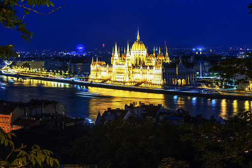 Fantastic Hungarian Parliament building in night illumination, small tourboat sails  nearby. Reflections in water of Danube river