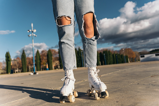 Young female skater’s legs in jeans stopped. Close-up image of a young woman’s legs wearing jeans and roller skates, with her feet on the ground static on the ground.