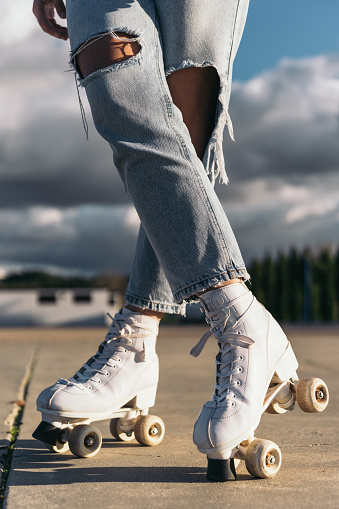 Young female skater’s legs in jeans and brake. Close-up image of a young woman’s legs wearing jeans and roller skates, crossing her feet and with one brake leaning on the ground.