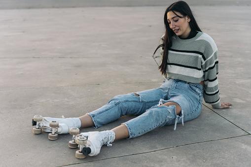 Portrait of a young Caucasian girl sitting on the ground with quad roller skates and ripped jeans looking defeated
