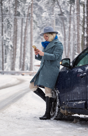 Woman waiting for assistance on a snowy road after car breakdown