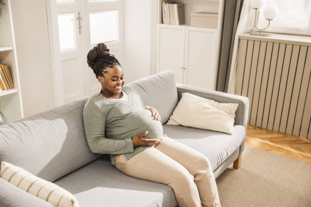 istock Happy pregnant  woman stroking belly while sitting on sofa 1971121664