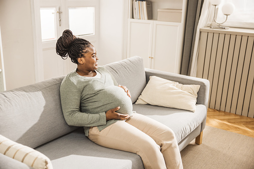 Happy pregnant  woman stroking belly while sitting on sofa