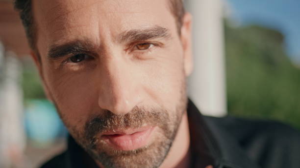 Attractive italian guy posing at sun beams square alone closeup. Portrait handsome bearded man looking camera confidently standing at plaza. Hot macho enjoying summer relaxing at greenery park nature