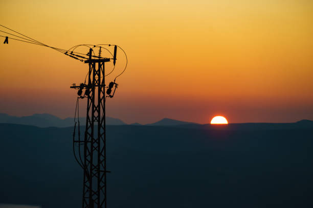 Coast with electricity transmission pylons, power lines high voltage towers. Sunset landscape in Spain