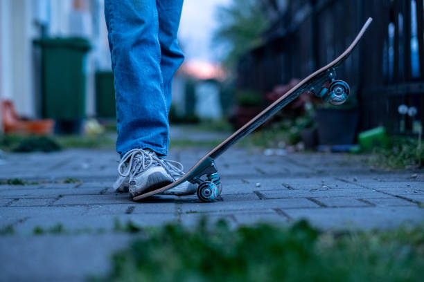 Skateboarder in baggy jeans holding scratched pink skateboard at city street. Teenager is skateboarding. Concept of youth subculture