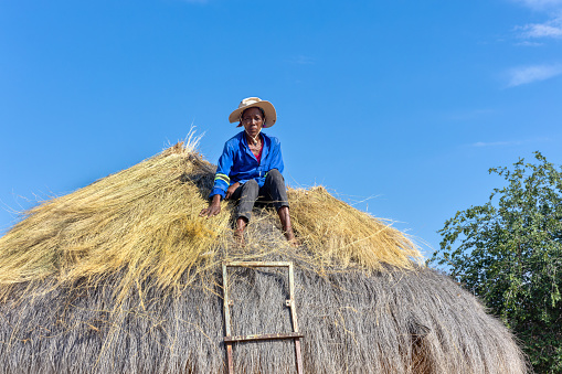 african woman climbed to repair a thatched roof on a hut