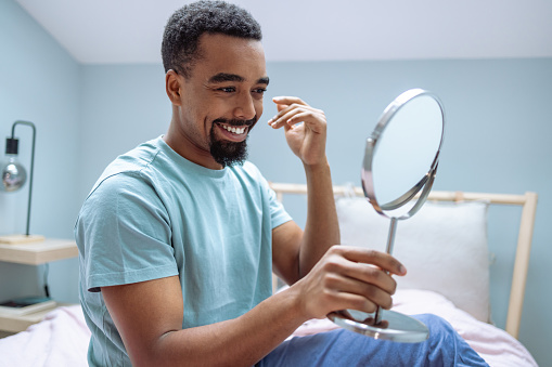 Photo of a satisfied man looks at himself in the mirror in the morning