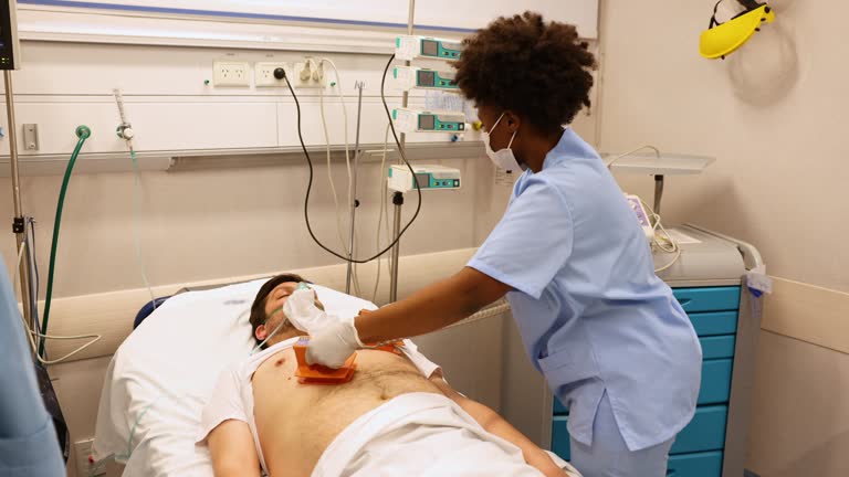 Black doctors trying to revive unconscious patient in emergency room using defibrillator and CPR