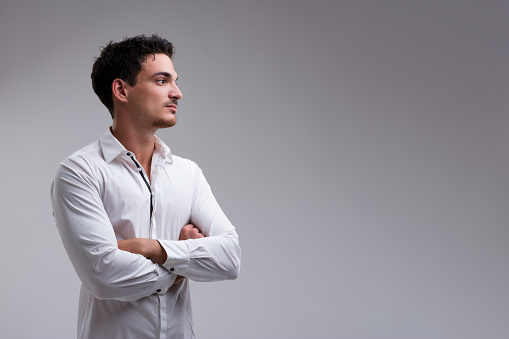 Proud, strong young man in white shirt with arms folded, gazes at something to his right within a wide copyspace. Short-haired, bearded, mustachioed, and tanned