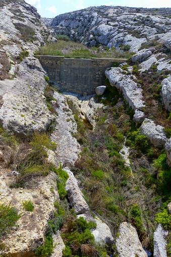 Artificial dam in a stone valley on the island of Gozo, a landscape with wild xerophytic vegetation, Malta