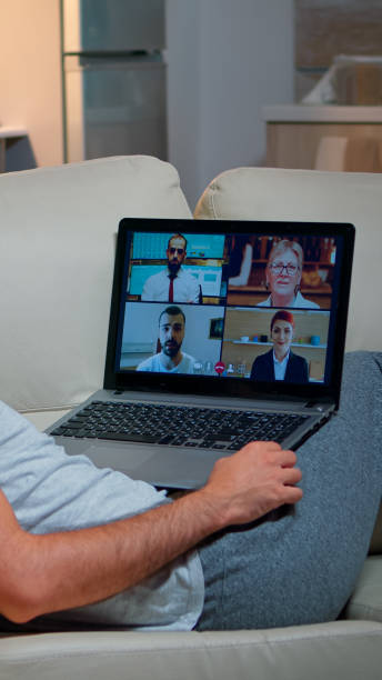 istock Tired man in pajamas sitting on sofa falling asleep while having online business videocall with teammates 1971386769