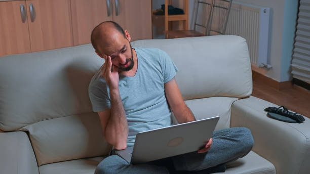 istock Tired man sitting on sofa while talking with collegue during business videocall conference 1971411882