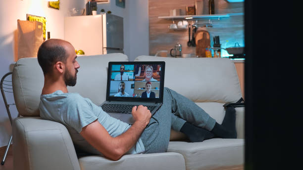 istock Business man in pajams lying on sofa while chatting with friends 1971413379