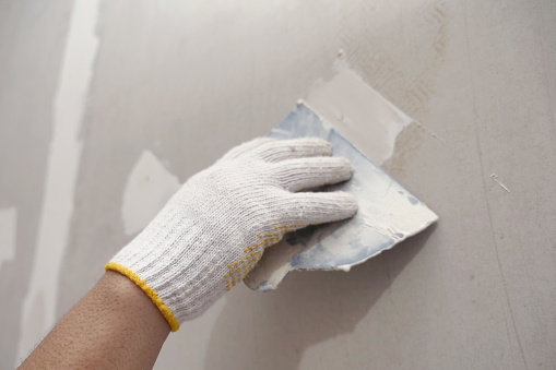 Plasterwork and wall painting preparation. close up hand of craftsman applying plaster or filling drywall patch