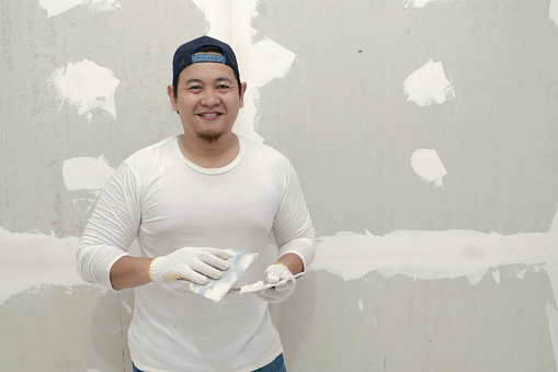 Happy Asian craftsmen smiling to camera, doing plasterwork and wall painting preparation.