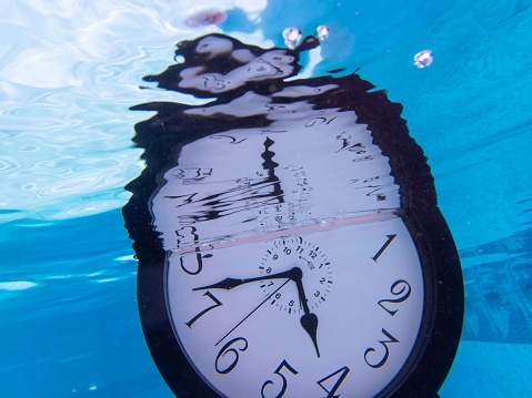 Lost time climate change concept drowning underwater clock in blue pool with distorted reflection. No people. with copy space.
