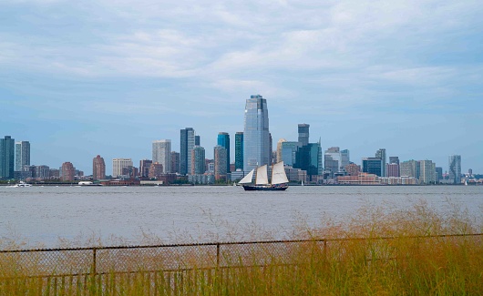 New York, NY, USA 09-19-2023 Beautiful cityscape with Hudson River and clipper sailing ship seen over tall grass from Governors Island. Editorial use only.