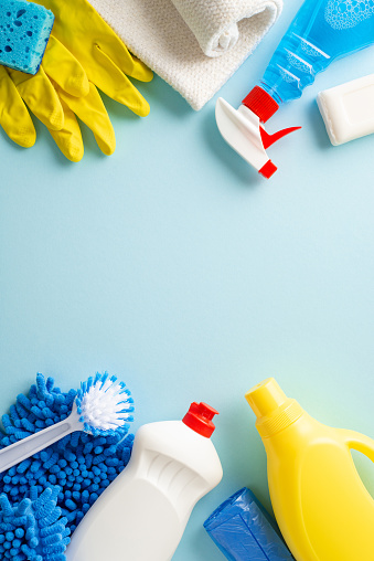 A clean sweep in aesthetics. Top view vertical photo featuring cleaning essentialsârags, gloves, and detergent bottlesâarranged on calming pastel blue background. Adaptable space for text or branding