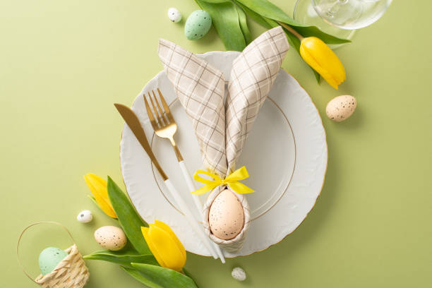 istock Springtime Table Ensemble: Elevate your Easter promotions with a top view of a table adorned with bunny ear napkin, cutlery, wine glass, tulips, small baskets with eggs on a pastel green backdrop 1971516078