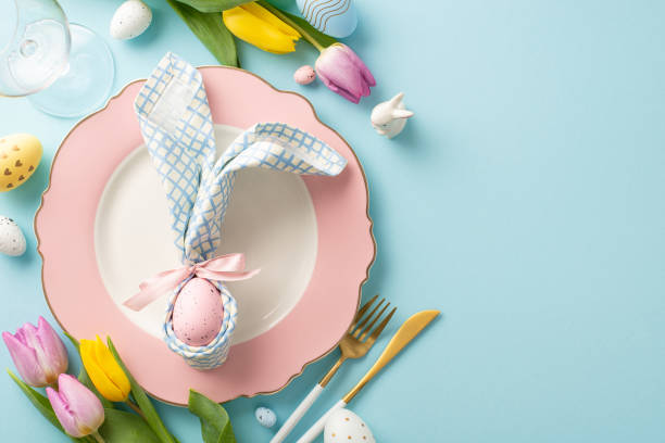 istock Spring Celebration Setup: Overhead shot of a festive table arrangement featuring a plate, bunny ear napkin, cutlery, wine glass, tulips, sugar sprinkles, eggs. Pastel blue backdrop with space for text 1971516330