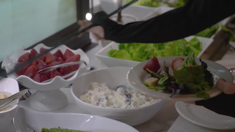 Up close shot of hands at salad bar putting food on plate