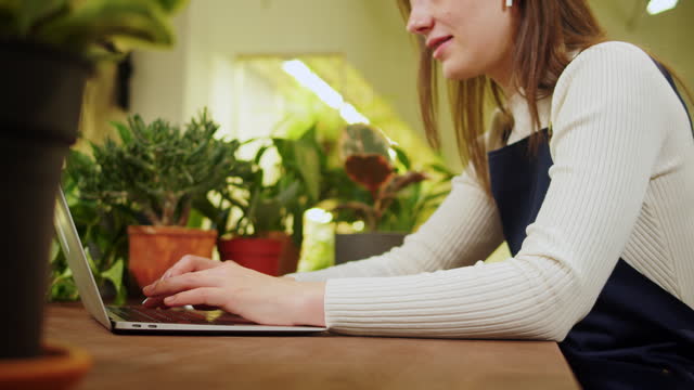 Florist woman using laptop. Greenhouse worker, female botanist typing on keyboard, small business owner. Gardener working in flower shop, plant store.