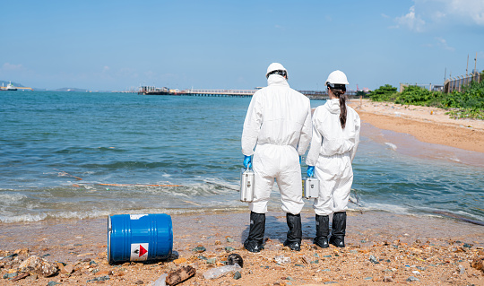 Scientists biologists and researchers in protective suits taking water samples from waste water from industrial. Experts analyze the water in a contaminated environment.
