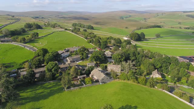 Moving, panning drone footage showing the beautiful village of Selside in rural Yorkshire, England with country lanes dry stone walls, hills, fields and mountains in the distance on a sunny summer day