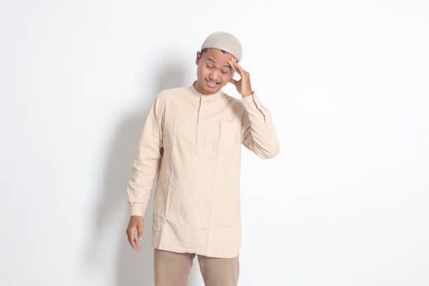 portrait of suffering asian muslim man in white shirt having a migraine, touching his temple. headache disease concept. isolated image on white background - pusing imagens e fotografias de stock