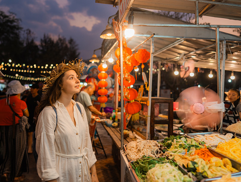Cheerful woman choosing food on night market during vacation