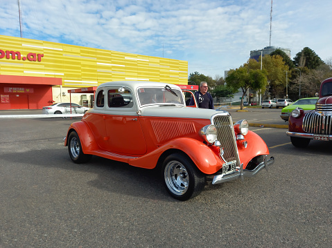 Buenos Aires, Argentina - Jun 4, 2023: Old white and orange 1934 Ford V8 model 40 coupe 5 window customized street rod in a parking lot. Classic car show. Sunny day