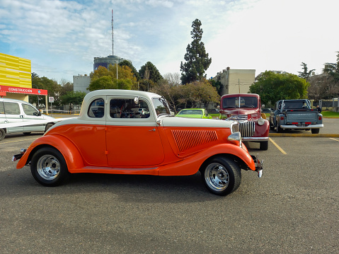 Buenos Aires, Argentina - Jun 4, 2023: Old white and orange 1934 Ford V8 model 40 coupe 5 window customized street rod in a parking lot. Classic car show. Sunny day. Side view