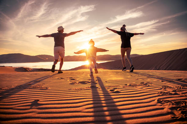 la famiglia felice con la figlia piccola corre nelle dune del tramonto - arid climate asia color image day foto e immagini stock