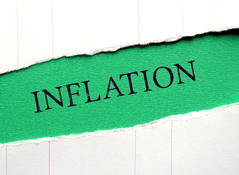 Words on green between torn white papers INFLATION, means increase in the prices of goods and services in economy- decreasing the purchasing power of money